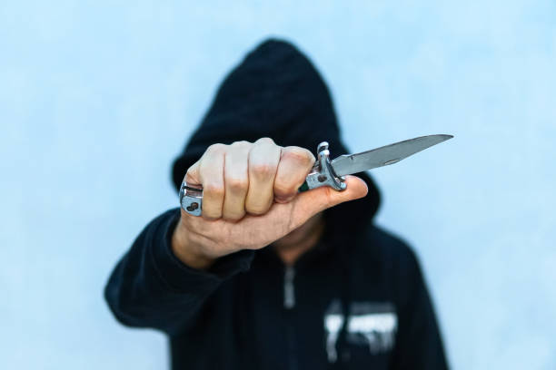 A young man in a hoodie holding A young man in a hoodie holding a knife symbolizing youth crime. Crime concept. The threat of a cold weapon. A terrorist from ISIS with a knife. A prisoner with a Shiv. assassination photos stock pictures, royalty-free photos & images