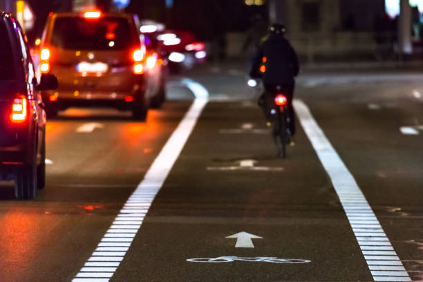 велосипедист едет по велосипедной дорожке мимо пробки - car speed lifestyles night стоковые фото и изображения