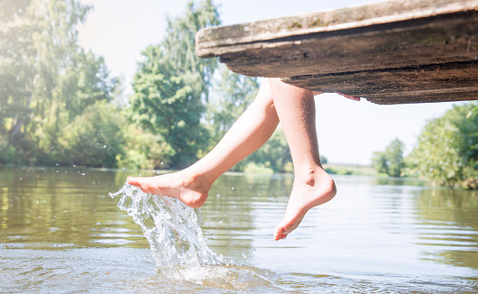 girl from the bridge sprays water legs, lifting splashes. Hot summer, soldechny day.