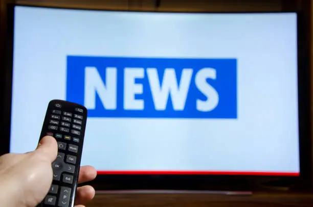 Photo of Man watching News on TV and using remote controller.