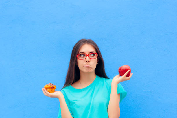 woman choosing between unhealthy muffin and healthy apple - choice thinking women decisions imagens e fotografias de stock