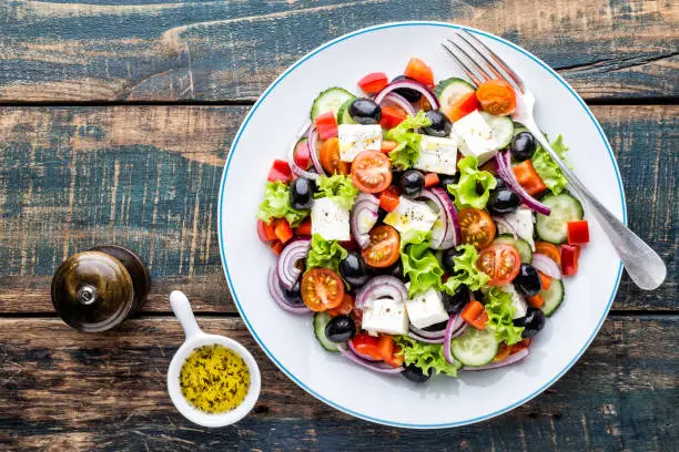 Photo of Greek salad of fresh cucumber, tomato, sweet pepper, lettuce, red onion, feta cheese and olives with olive oil. Healthy food, top view