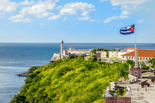 испанская крепость эль-морро с маяком, пушками и кубинским флагом на переднем плане, с морем на заднем плане, гавана, куба - havana стоковые фото и изображения