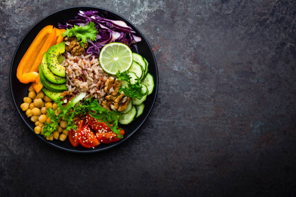 istock Buddha bowl dish with brown rice, avocado, pepper, tomato, cucumber, red cabbage, chickpea, fresh lettuce salad and walnuts. Healthy vegetarian eating, super food. Top view 927355566
