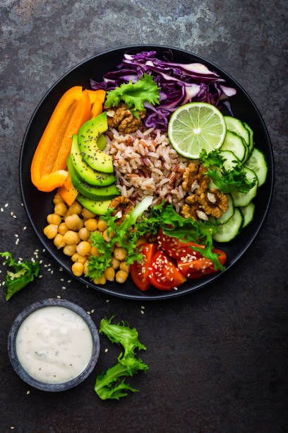 istock Buddha bowl dish with brown rice, avocado, pepper, tomato, cucumber, red cabbage, chickpea, fresh lettuce salad and walnuts. Healthy vegetarian eating, super food. Top view 927355578