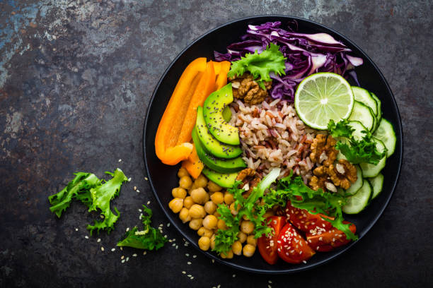 istock Buddha bowl dish with brown rice, avocado, pepper, tomato, cucumber, red cabbage, chickpea, fresh lettuce salad and walnuts. Healthy vegetarian eating, super food. Top view 927355582