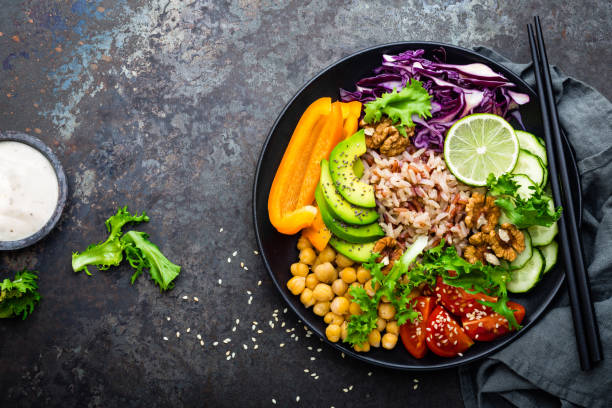 istock Buddha bowl dish with brown rice, avocado, pepper, tomato, cucumber, red cabbage, chickpea, fresh lettuce salad and walnuts. Healthy vegetarian eating, super food. Top view 927355672