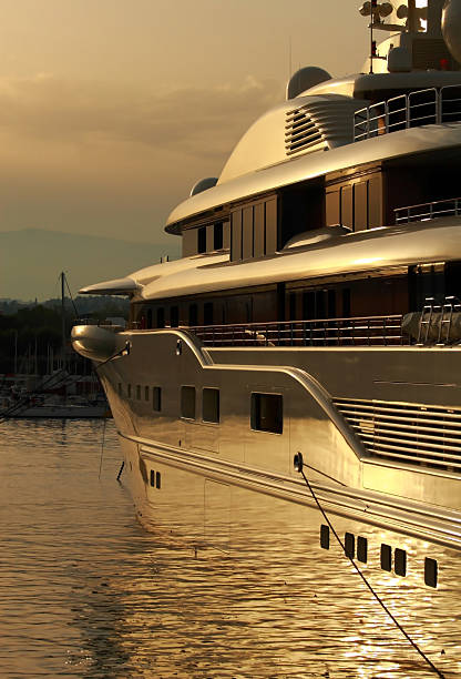 Picture of the Bosporus straight in Istanbul, Turkey, with luxury yachts cruising. A sleek motor yacht plows through sunflecked waters on Istanbul's Bosphorus Strait, leading a small flotilla toward the Sea of Marmara while bulk carriers and ferries anchor in the hazy distance. The Asian shoreline curves along the right margin, its green hillsides dotted with villas, seaside parks and whitewashed minarets, whereas silhouettes of the Historic Peninsula line the far horizon to the left. Rippling wakes, backlit spray and gentle morning glare evoke the vibrancy of summer navigation on one of the world's busiest natural waterways, underscoring Istanbul's dual identity as both leisure playground and global trade corridor linking Europe with Asia.