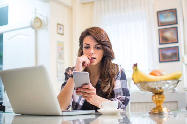 giovane donna nervosa che guarda lo smartphone e si morde le unghie a casa. - staring foto e immagini stock