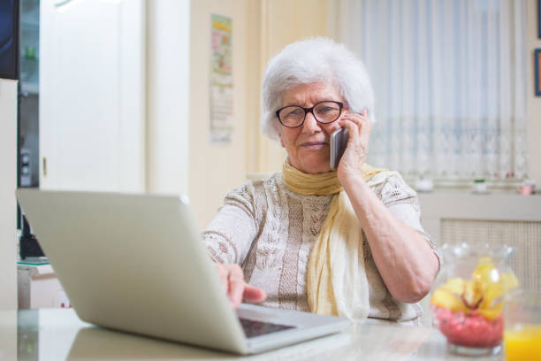 istock Smiling senior woman using phone and laptop at home. 927375272