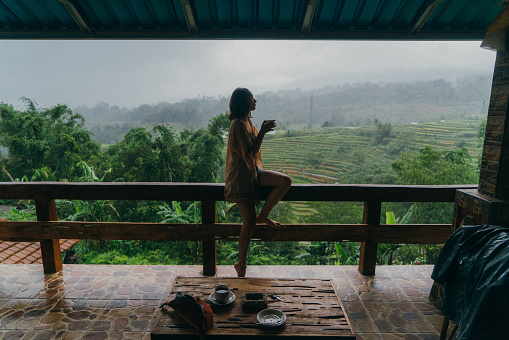 Young Caucasian woman  drinking tea on balcony with view  on rice fields in Bali, Indonesia