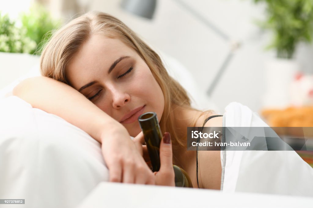 Lonely young woman sleeps early in the morning Lonely young woman sleeps early in morning at home embrace with bottle of wine in bedrooms bed with white sheets Drowning Stock Photo