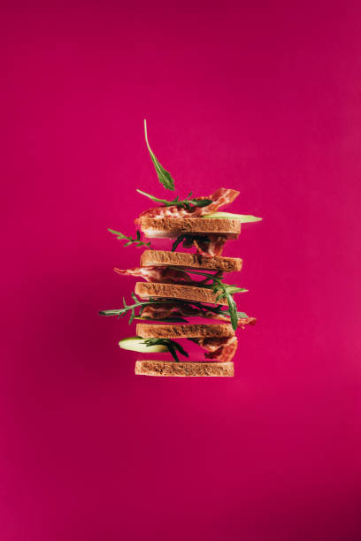 ベーコン ピースとピンクの分離したルッコラのサンドイッチを空中浮揚のクローズ アップ表示 - フードデザイン ストックフォトと画像