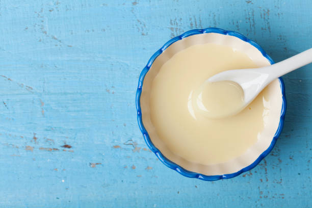 Condensed milk or evaporated milk in bowl on blue table top view. stock photo