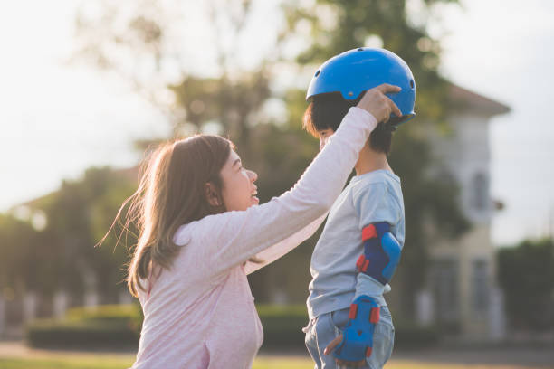 asia madre ayudando a su hijo lleva casco azul a disfrutar tiempo juntos en el parque - ropa protectora deportiva fotografías e imágenes de stock