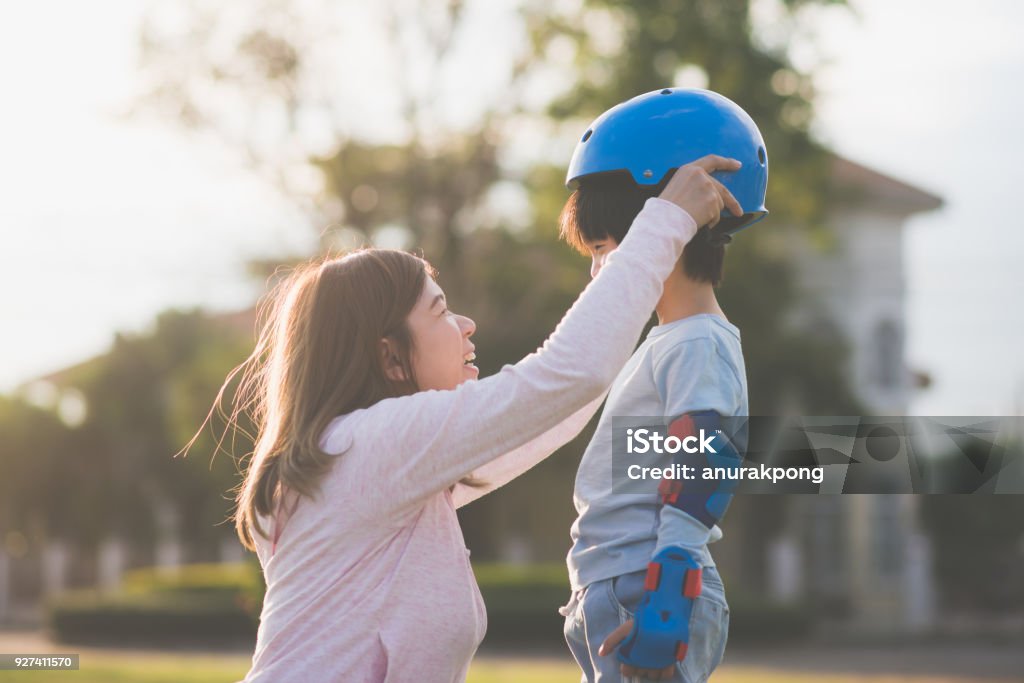 그녀의 아들을 돕는 아시아 어머니 블루 헬멧에 착용 즐기는 시간 함께 공원에서 - 로열티 프리 보호 스톡 사진