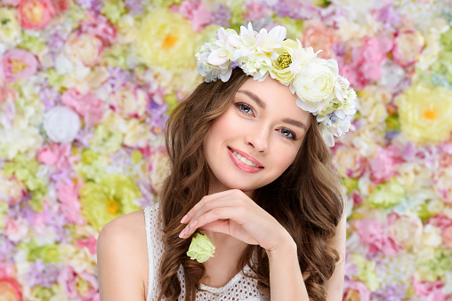 smiling young woman in floral wreath with blossoming rose bud