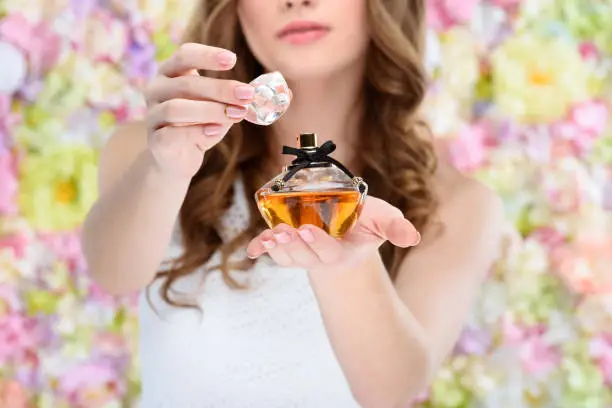 Photo of cropped shot of woman opening bottle of perfume on floral background