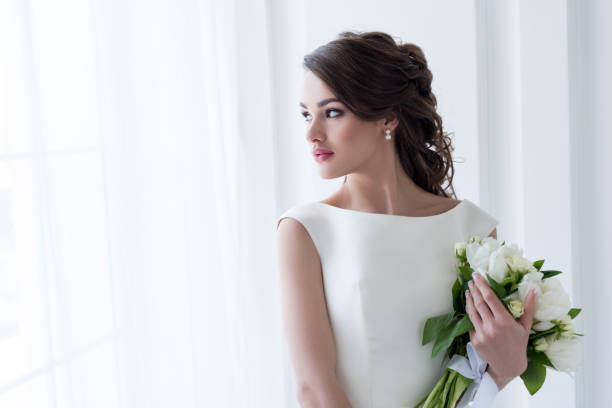 istock beautiful bride holding wedding bouquet and looking at window 927421590