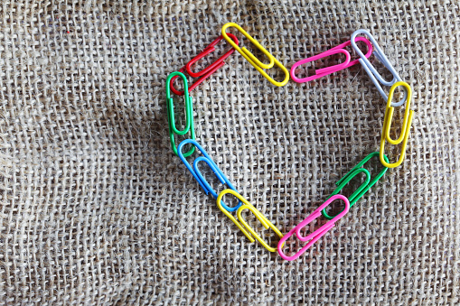 close up of colorful paper clips arranged in heart shape sign on sack cloth background