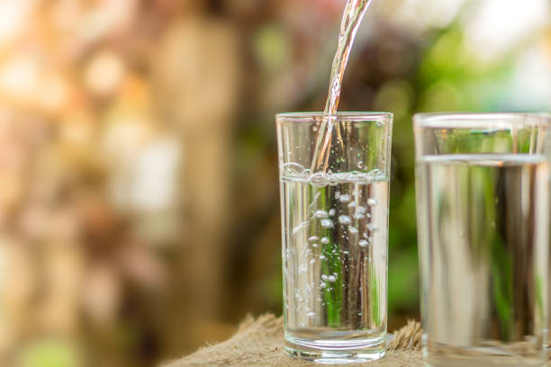 pouring fresh water on drinking glass over nature sunlight morning background - copo imagens e fotografias de stock