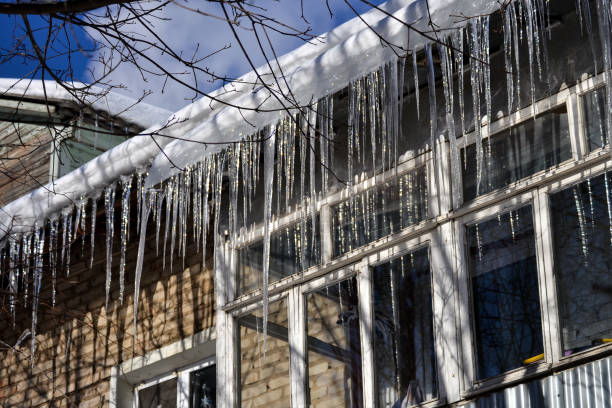 istock Large, sharp icicles hang from the roof. Dangerous icicles on the roof. 927436462