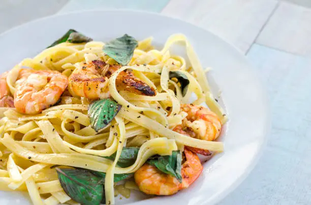 Pasta with prawns and basil leaves on white plate.