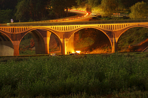 night scene of bridge and people camping place with fire in the summer. Romania;