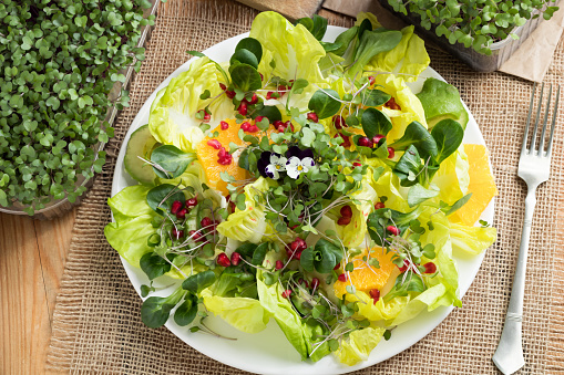 Vegetable salad with fresh kale and broccoli microgreens, lettuce, corn salad, pomegranate, orange, avocado and edibe flowers, top view