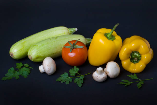 istock Yellow peppers with zucchini and tomatoes on a dark background. Composition from different vegetables on a dark background. White mushrooms with peppers and tomatoes. 927459636