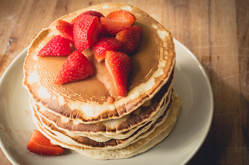 A stack of homemade pancakes on a white plate with cut strawberries on top. Landscape format.
