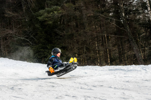 A child riding a sledge downhill and jump in mid air. stock photo