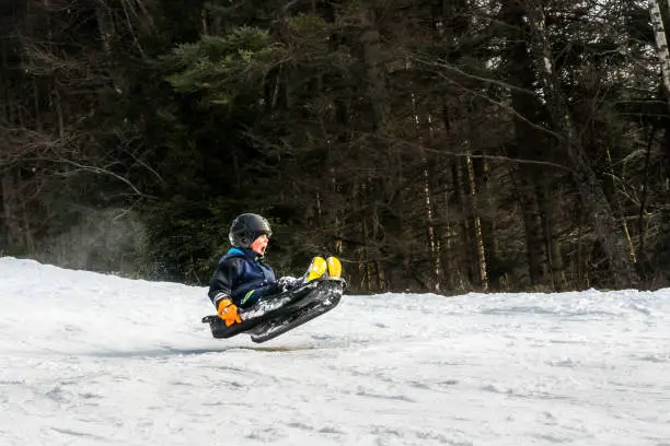 Winter snow activity. A child riding a sledge downhill and jump in mid air.