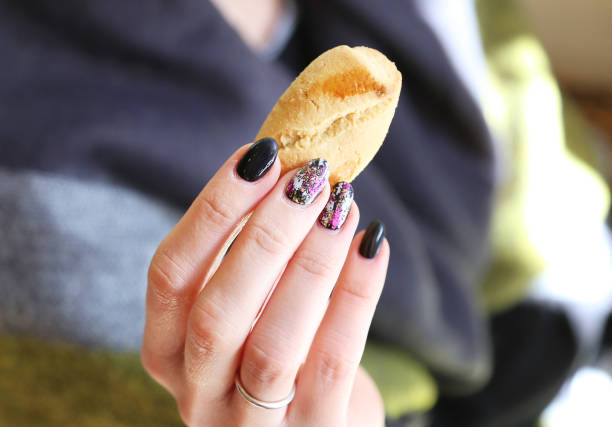 woman hands with beautiful manicure holding a cookie - black polish with designed fashion shapes stock photo