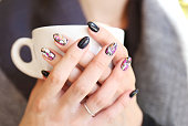 woman hands with beautiful manicure holding a cup of coffee - black polish with designed fashion shapes