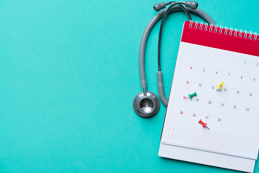 Top view of stethoscope and calendar on the green background, schedule to check up healthy concept