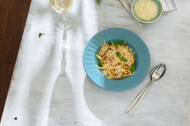 prato de macarrão à carbonara com copo de vinho branco na mesa de madeira branca, vista superior. conceito de mesa de jantar - food and drink cheese grated bowl - fotografias e filmes do acervo