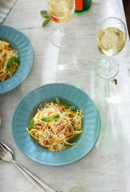 mesa de jantar. top ver os dois prato de macarrão à carbonara com copo de vinho branco na mesa de madeira branca - food and drink cheese grated bowl - fotografias e filmes do acervo