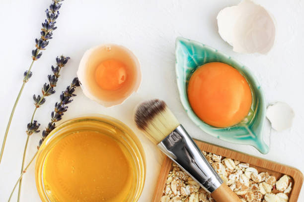 Bright egg yolks, oatflakes, honey, lavender with cosmetic brush closeup, natural holistic ingredients for homemade beauty care. Fresh products for glowing skin. White background viewed above. botanical spa treatment stock pictures, royalty-free photos & images