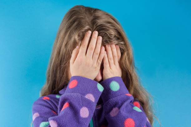 istock A child girl covered her face with hands, on a blue studio background. 927516588