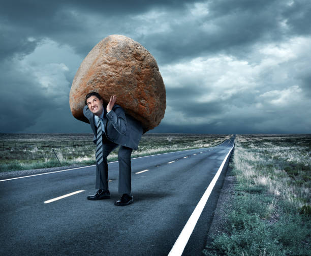 istock Businessman Struggles To Carry Large Boulder On His Back Down Rural Road 927521436