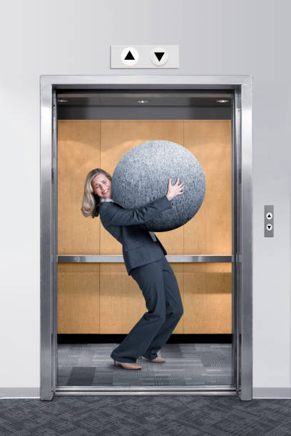 istock Businesswoman Struggles To Carry Large Stone In An Elevator 927530074