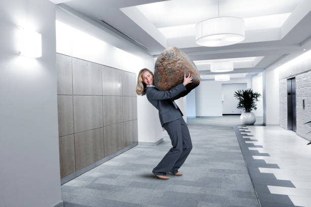 istock Businesswoman Struggles To Carry Large Stone In Office Setting 927530086
