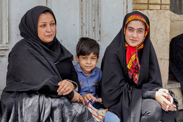 Islamic family, two women and a small boy, Kashan, Iran. Kashan, Iran - April 27, 2017: A Muslim family, two women and one young boy, are waiting for the municipal bus at a public transport stop. iranian culture stock pictures, royalty-free photos & images