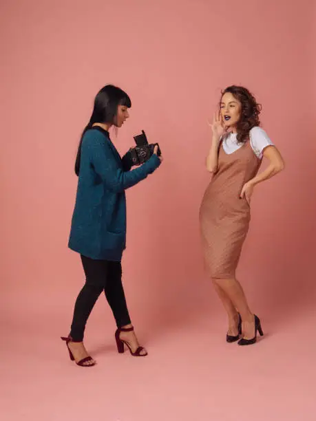 Photo of Girl photographer takes pictures of model on pink background in studio with retro film camera