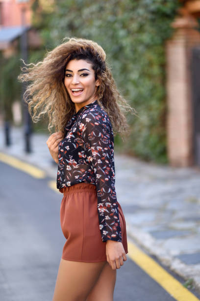 Happy young arabic woman with black curly hairstyle. Happy young arabic woman with black curly hairstyle. Arab girl smiling in the street moving her hair. street fashion stock pictures, royalty-free photos & images