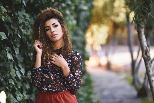 Beautiful young arabic woman with black curly hairstyle. Arab girl wearing casual clothes in the street.