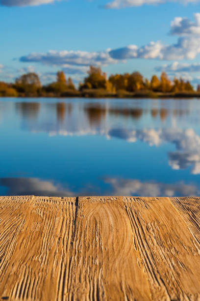 istock Empty rustic wood table top on  blurred colorful autumn landscape background with fall forest and blue sky with cloudscape reflection on the lake. Can montage or display your products 927561166