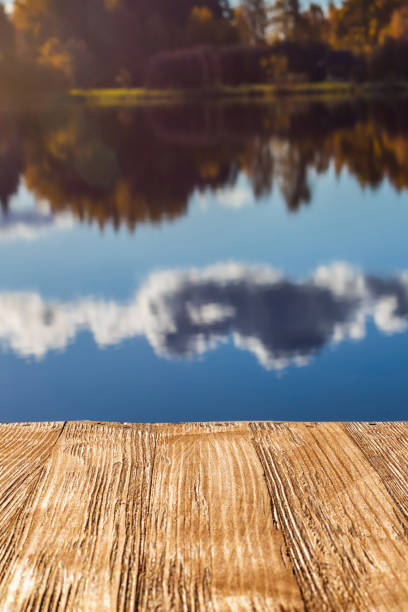 istock Empty rustic wood table top on  blurred colorful autumn landscape background with fall forest and blue sky with cloudscape reflection on the lake. Can montage or display your products 927561230