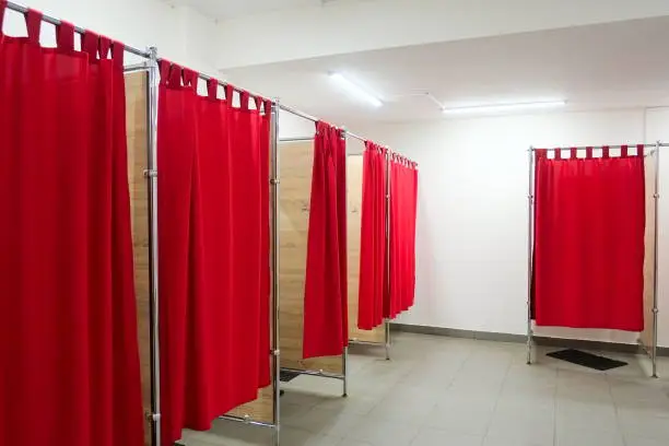 Empty fitting rooms with red curtains and white walls. Dressing rooms in clothing store.